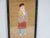 A three-dimensional textile art of an Oriental male figure. It is professionally framed behind glass, mounted on a tan...
