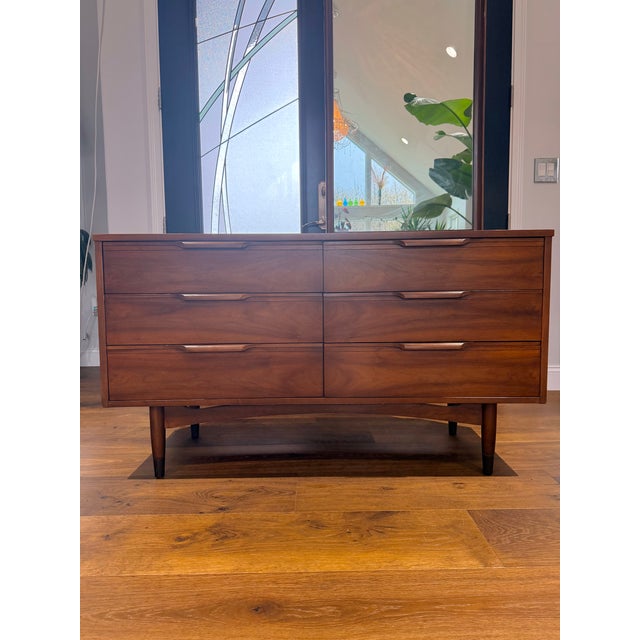 A stunning vintage mid-century modern walnut dresser featuring clean lines, sculpted drawer pulls, and beautifully grained...