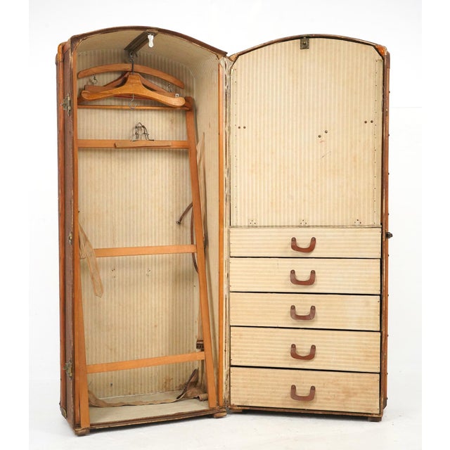 Antique steamer wardrobe trunk with an internal wood frame and braces, a brown coated fabric surface, and a leather handle...