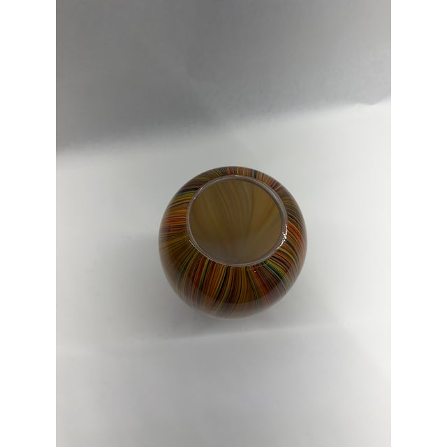 A hand-blown art glass vase featuring an intricate array of fine vertical glass canes in rich amber, orange, yellow, and...