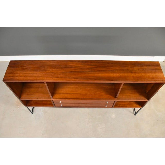 A mid century modern walnut bookcase with l shelves sitting on an iron base made by Stanley Furniture. Can he make...