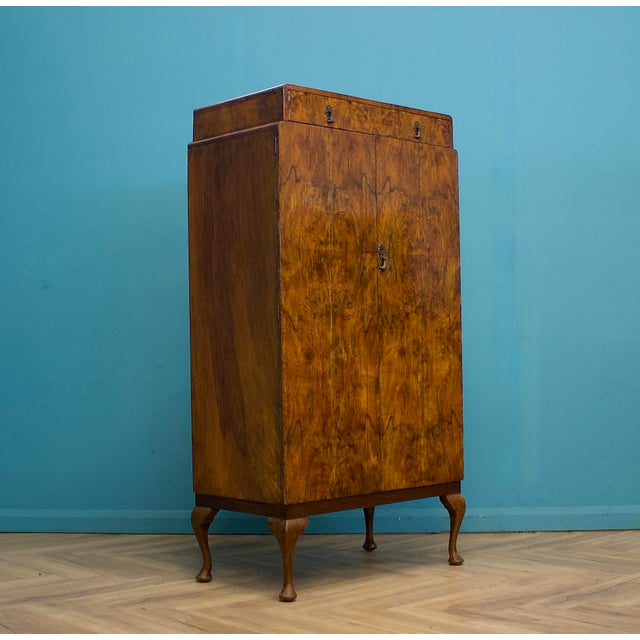 A compact vintage wardrobe in an early 20th-century style, displaying beautifully figured warm wood veneer with a strong,...