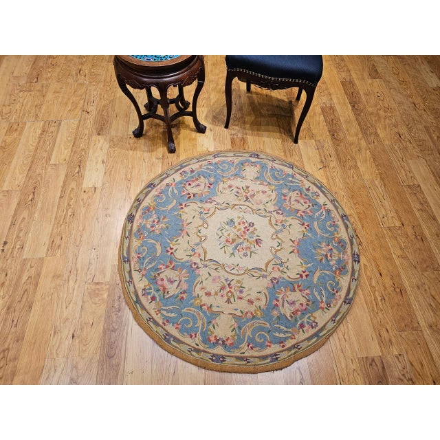 This vintage round needlepoint rug features an elegant floral design in red, green, brown, and ivory set against a crisp...