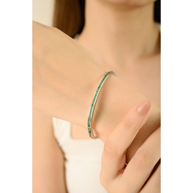 This elegant bangle bracelet is crafted in 925 sterling silver and adorned with 36 vibrant, square-cut emeralds weighing a...