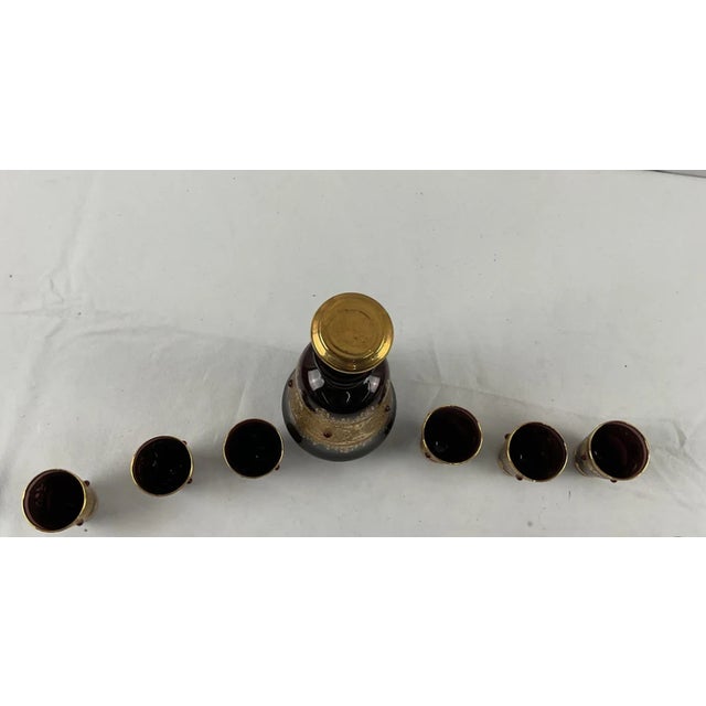 DESCRIPTION A seven-piece liquor set in deep burgundy glass: one tapered, bell-shaped decanter with a stopper and six...