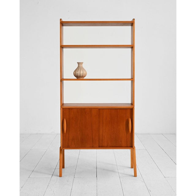 Vintage Scandinavian teak bookcase. Featuring open shelves, a storage compartment with sliding doors, and tapered legs....