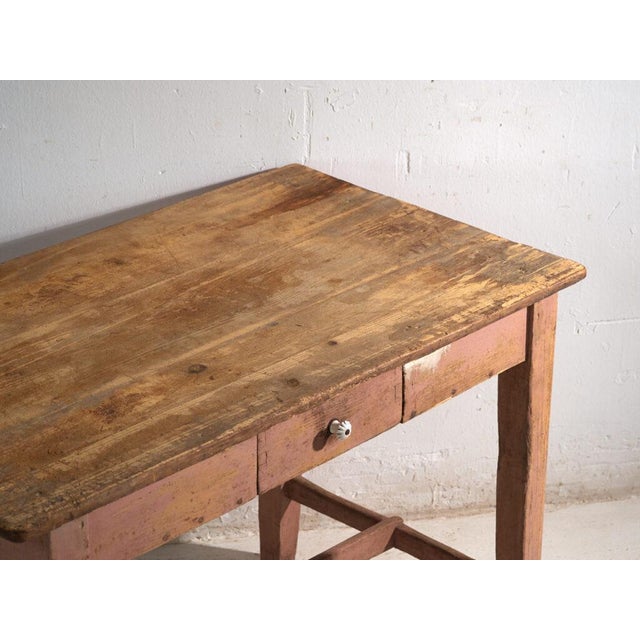 This antique kitchen table in pine wood carries a frieze drawer with a porcelain knob and stands on four squared legs tied...
