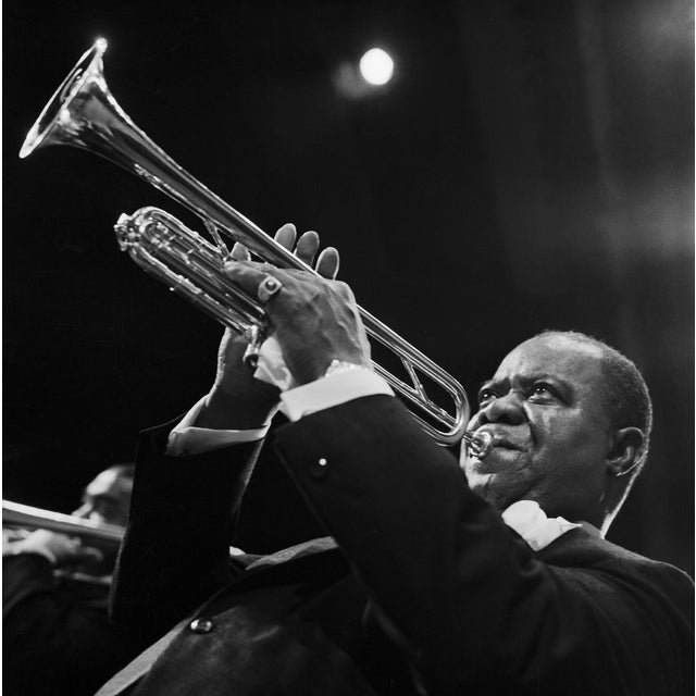 This black-and-white photo captures jazz legend Louis Armstrong playing his trumpet during a performance in Berlin in...