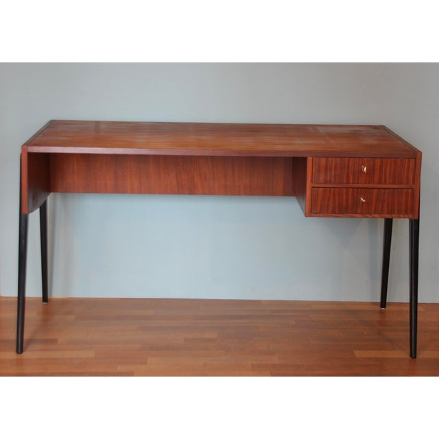 A very elegant desk from the 1960s. The desk's frame is made of teak, and the tapered, slightly angled legs are painted...