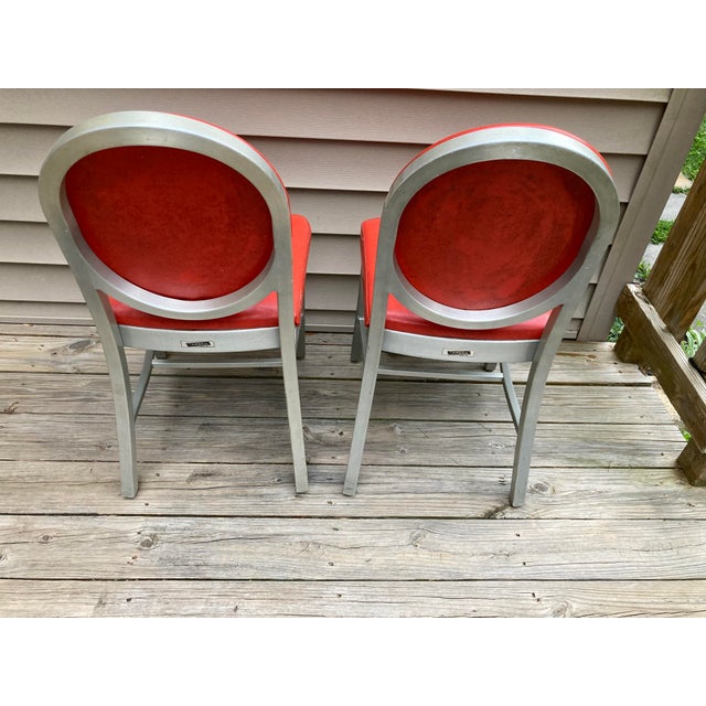 Pair of iconic vintage, untouched Emeco padded round back aluminum chairs. Both labels intact. Red vinyl in decent, usable...