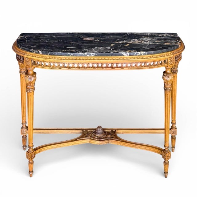 A Louis XVI style demilune console table having a recessed top of arresting polished Portoro Nero marble with caramel and...