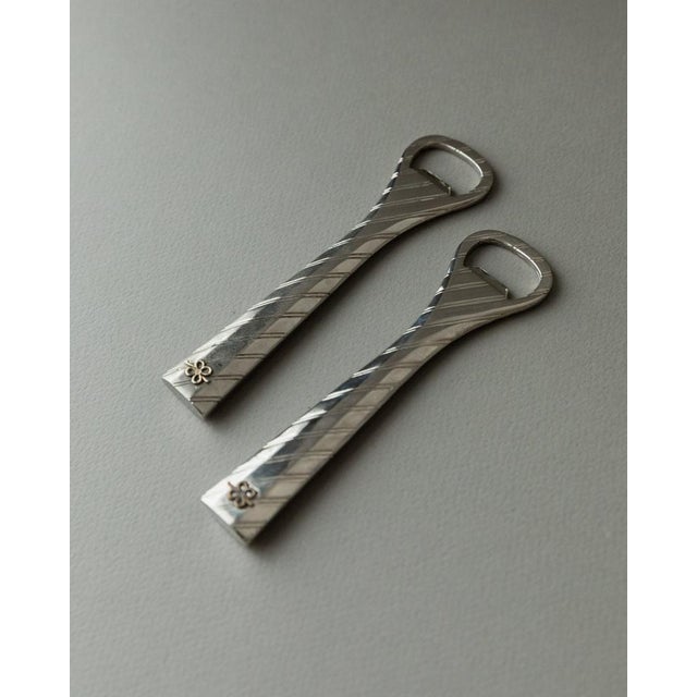 This elegant set of two silver-plated bottle openers in a timeless 1960s design features a striped relief and bow details....