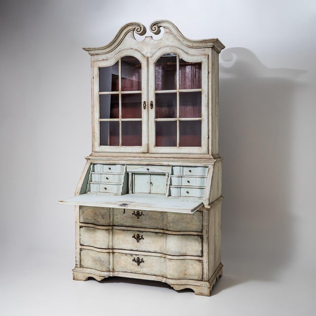 Elegant secretary desk with glazed upper cabinet and a gracefully broken arched pediment. The softly patinated finish in...