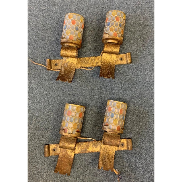 A pair of Spanish mid-century gilt hand hammered iron brutalist electric wall sconces with multi-colored reticulated glass...