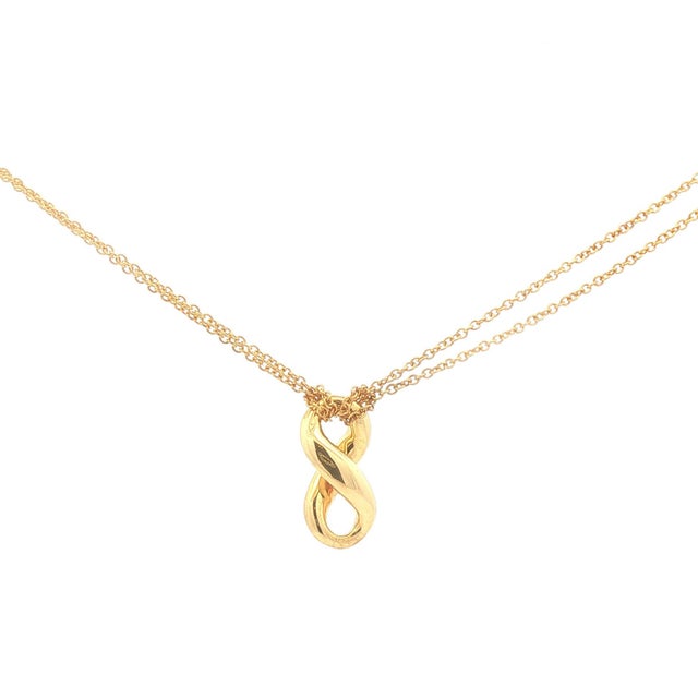 An 18k gold pendant necklace by Tiffany & Co. The pendant features a twisted infinity design, suspended on a delicate...