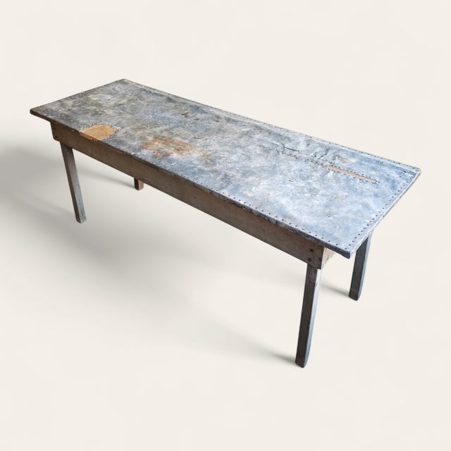 A long early 20th-century American primitive worktable featuring a beautifully weathered zinc top over a painted wooden...