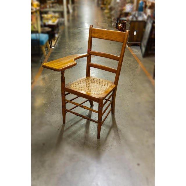 A circa 1930s wooden school chair with a caned seat and attached writing desk, showcasing vintage charm and functional...