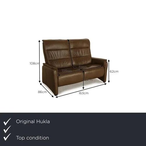 The two-seater Hukla is covered with brown genuine leather and stands on small black feet. It is characterized by the...