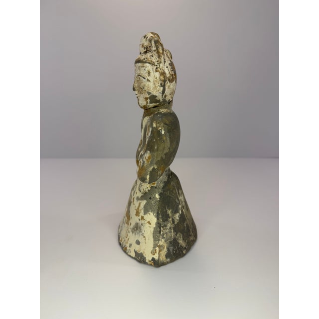 Small statuette featuring a person kneeling, clothed in a robe crossing at the chest, with arms folded and hands covered....