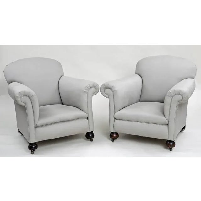Pair of large club chairs with rounded backs, outwardly scrolled arms, tight seat, raised on beech bun feet on casters,...