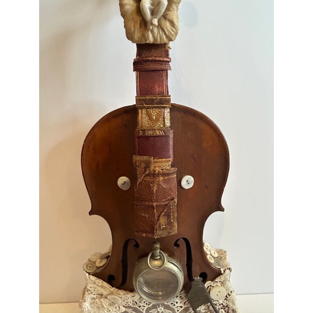 Imaginative wall sculpture created on a vintage violin where the instrument’s shape suggests a baby’s figure wrapped in...