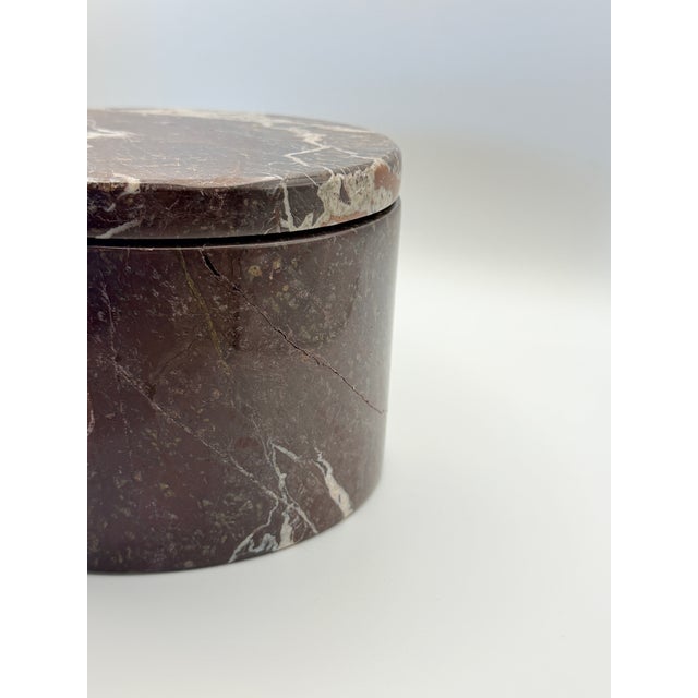 A substantial round keepsake box crafted from richly veined Red Zebra marble, featuring deep burgundy, rust and cream...