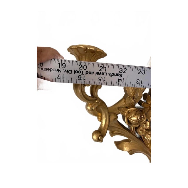This vintage Syroco sconce features an elegant gold tone finish with intricate floral detailing and a decorative bow at...