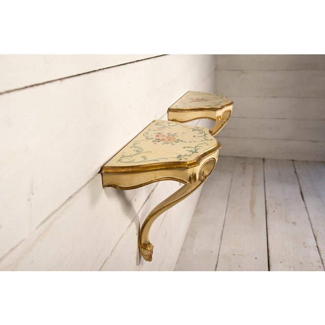 The half-moon console tables are made of painted wood. The ivory-white base features gold trim and moldings. The...