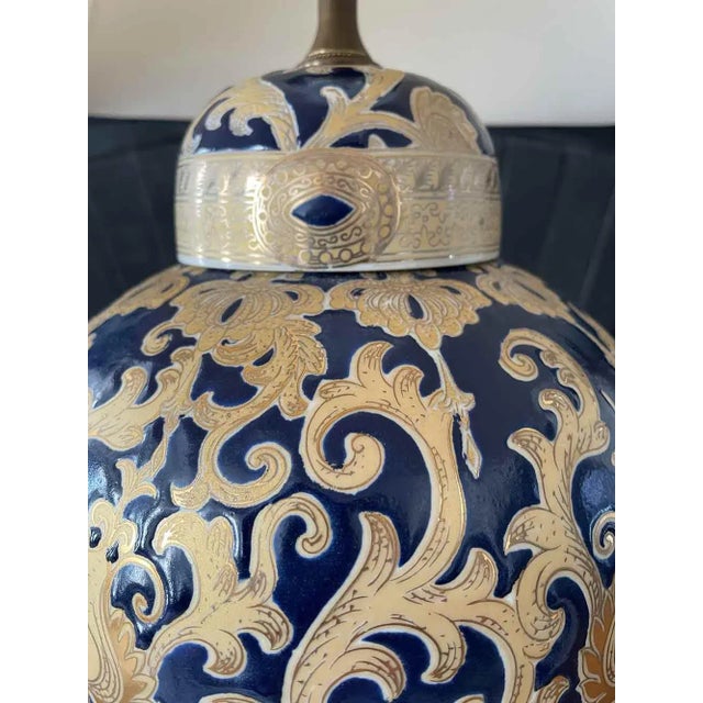 Vintage deep blue and gold scroll design table lamp. Ceramic lamp sits on a wooden base with an off white shade. Shade...