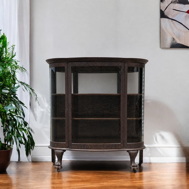 A vintage oak bow-front display cabinet with curved glass on three sides, sculptural claw feet and a compact 49-inch-wide...