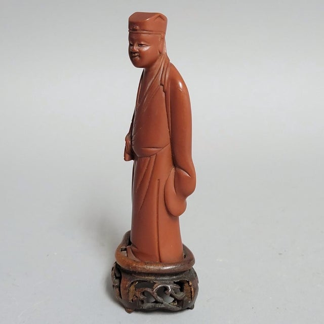 A finely modeled early 20th-century Chinese export figure of a scholar, carved from an opaque cinnamon-toned resin...