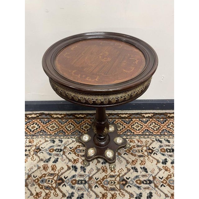 A beautifully crafted round pedestal table featuring intricate inlay work, elegant brass detailing, and charming miniature...