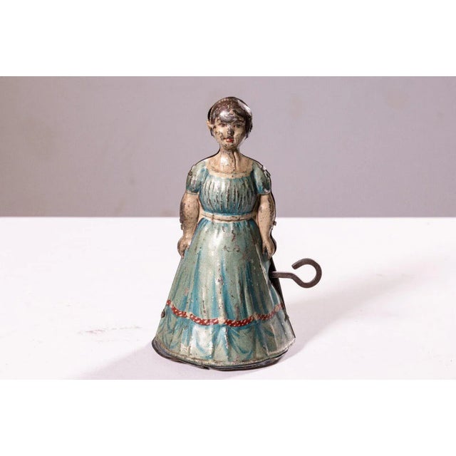 An antique windup tin toy depicting a woman or maid in an apron designed by Heinrich Fisher & Co. When the toy is wound...