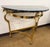 A stylish brass demilune console table with a black marble top and distinctive horse-head supports, offering a...
