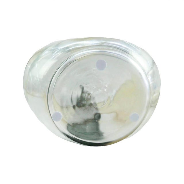 The smooth, rounded silhouette is crafted from clear glass and layered with soft, abstract swaths of muted green and warm...