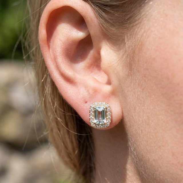 Exude tranquil beauty with these delicate halo stud earrings, featuring an emerald-cut natural light aquamarine defined by...