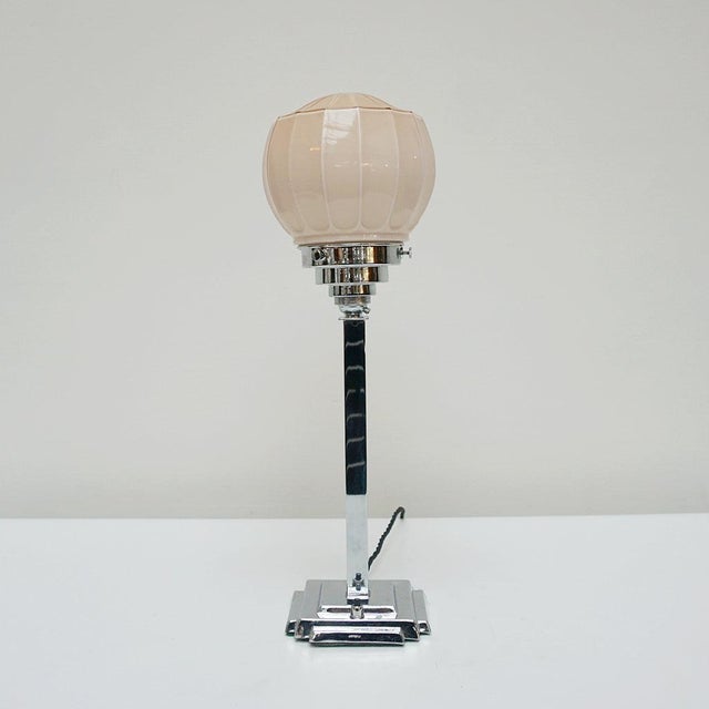 An original art deco table lamp. Chromed stem with ornate peach pink glass globe shade. Dimensions: h 46cm w 12cm origin:...
