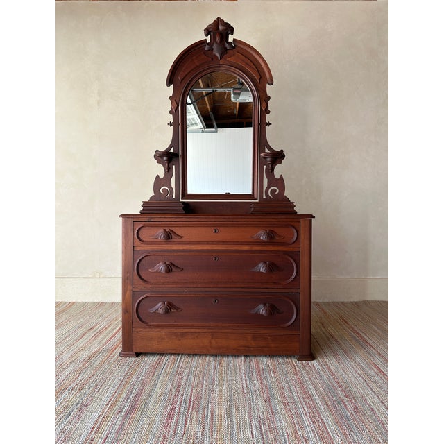 This antique wooden dresser features an impressive arched mirror, sculpted drawer pulls, three generous drawers, and a...