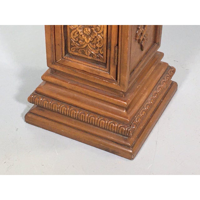A carved wooden pedestal cabinet in a rich walnut finish with an inset marble top, gadrooned molding, single door, finely...