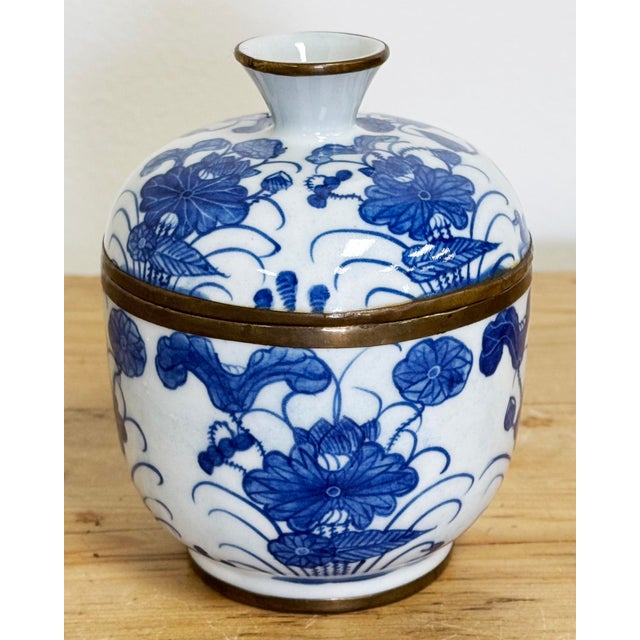 Vintage porcelain vibrant blue and white floral motif lidded jar. Brass strip at frame and handle. Patina to brass. No...