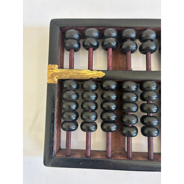 This vintage wooden abacus showcases a traditional design with a dark-stained frame, black counting beads, and brass...