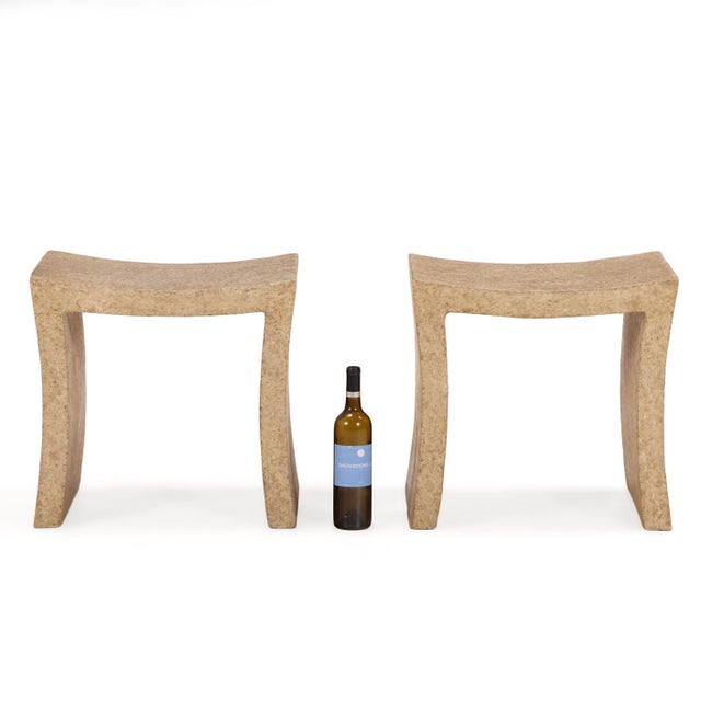 Each stool features a minimal, organic silhouette defined by a concave, saddle-form seat bridging two wide, subtly tapered...