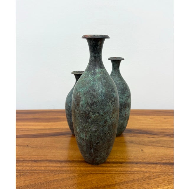 A handsome set of three vintage bronze decorative vases featuring elegant bottle-form silhouettes with naturally tapered...