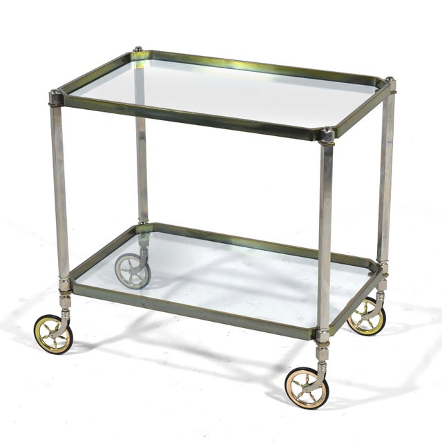 This serving cart or bar cart has an elegant simplicity. The metal frame supports two glass tops and rolls freely on...