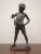 A decorative bronze statue representing a standing boy in a slightly relaxed posture, with his head tilted to his right...