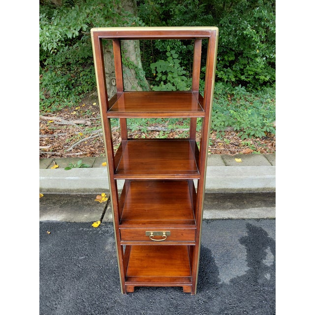 A classic Baker Furniture campaign-style étagère crafted in rich mahogany with solid brass corner accents and hardware....