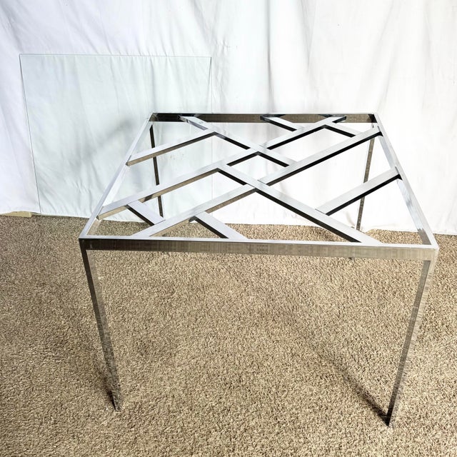 A striking Mid Century Modern table featuring a geometric chrome lattice base beneath a clear glass top. The sleek,...