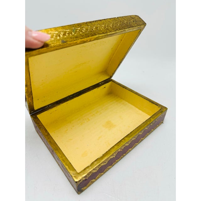 A decorative Napoleon-style keepsake box with a regal, French Empire look. The rectangular box features a deep red faux-...