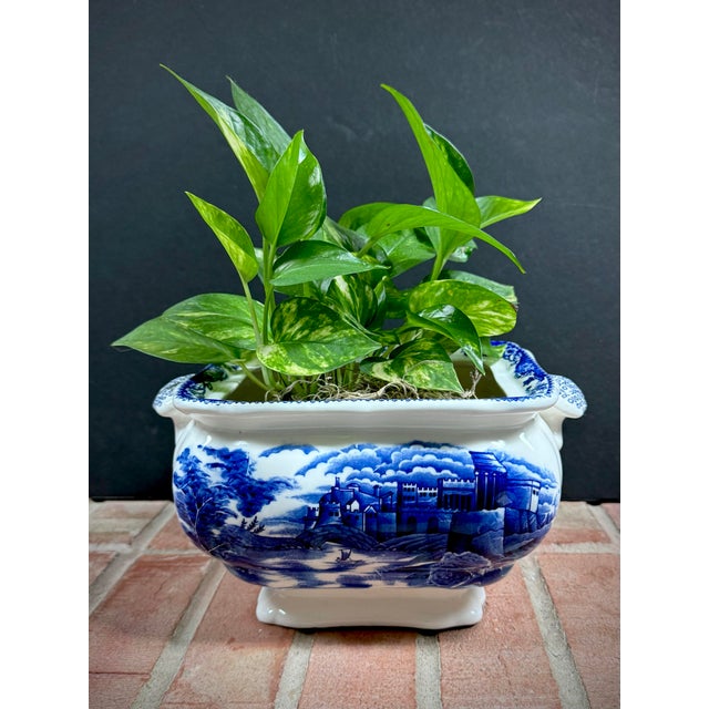 This vintage earthenware cachepot features a cobalt blue transfer ware pattern depicting a castle, bridge, and river scene...