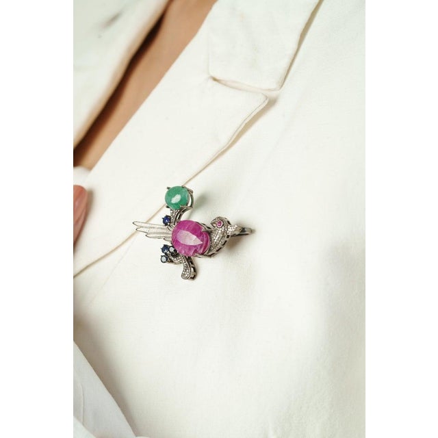 This exquisite 925 sterling silver brooch cum pendant showcases a charming bird-inspired design adorned with GF-blue...